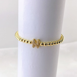 Vista macro de pulsera de cuentas doradas con colgante letra M en micro circonitas