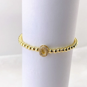 Primer plano de pulsera de cuentas doradas con un dije de letra O con micro pavé