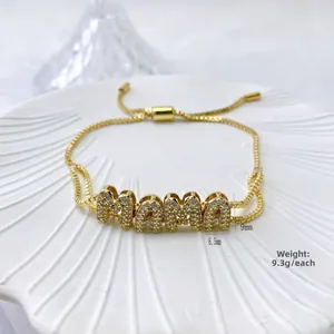 Detail of gold MAMA letter bracelet with cubic zirconia on a white shell plate