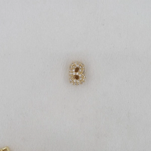 Macro shot of letter B gold pendant with pavé cubic zirconia on fabric background