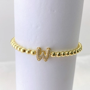 Vista macro de pulsera elástica de cuentas doradas con colgante letra W y circonitas