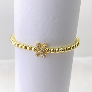 Primer plano de pulsera dorada de cuentas con dije de mariposa micro-pave en base blanca