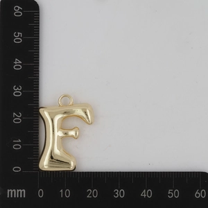 Vue macro du pendentif lettre F dorée gonflée avec surface polie sur une règle graduée