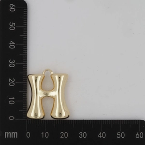 Vue macro du pendentif lettre H doré avec finition polie et outil de mesure de taille