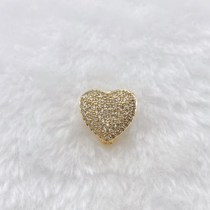 Detail of a golden heart charm with sparkling pavé crystals on white plush background