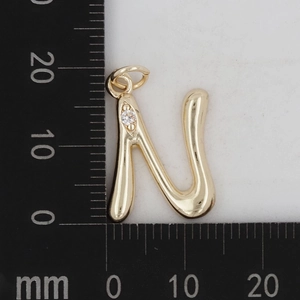 Nahaufnahme vom goldenen Buchstaben-N-Anhänger mit Zirkon auf einem Millimetermaß