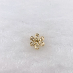 Macro view of a gold flower charm with white zircons on a white plush background
