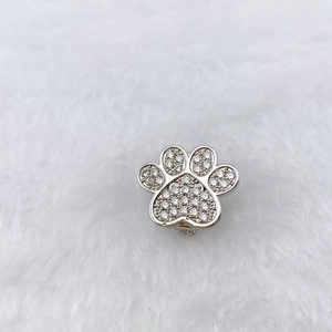 Macro shot of silver paw pendant with cubic zirconia inlay on white faux fur background
