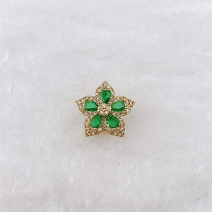 Macro detail of a gold flower charm featuring pear-shaped green stones and white pavé zircons