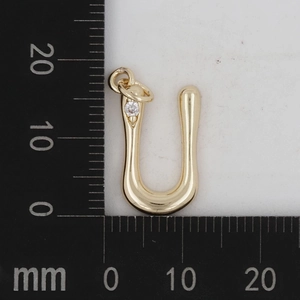 Makroaufnahme eines goldenen U-Messinganhängers mit Lineal und Zirkon-Inlay-Detail