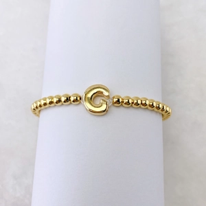 Detailaufnahme eines vergoldeten Perlenarmbandes mit einem großen Buchstaben-G-Anhänger