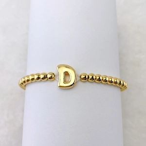Detail eines 18k vergoldeten Perlenarmbands mit einem polierten Buchstaben D Anhänger