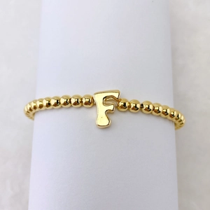 Detailaufnahme der goldenen Perlenarmband mit einem 18k vergoldeten Anhänger Buchstabe F