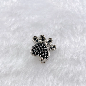 Macro detail of a silver cat paw charm with black zircons on white plush background