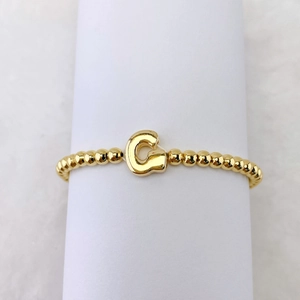Detail eines 18k vergoldeten Perlenarmbandes mit einem großen Buchstaben G Anhänger