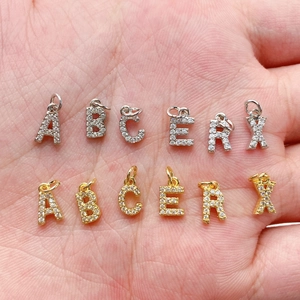 Mini ciondoli con lettere in zircone oro e argento mostrati nel palmo della mano