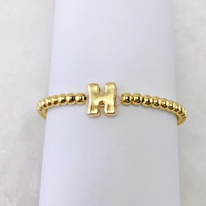 Makroansicht der 18k vergoldeten Perlenarmband mit einem großen Metall-H-Anhänger-Detail