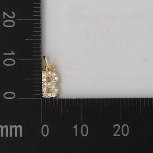 Vista macro del ciondolo lettera B dorata da 10 mm con pavé di zirconi su una scala