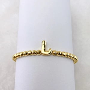 Makro-Detail des 18k vergoldeten Perlenarmbands mit einem blasenförmigen Buchstaben-L-Anhänger