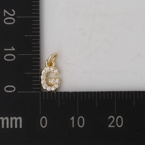 Macro di un ciondolo lettera G dorata con zirconi bianchi e scala graduata 10mm