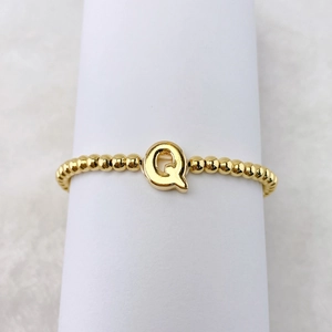 Detail eines 18k vergoldeten Perlenrings mit einem 3D-Buchstaben-Q auf weißem Halter