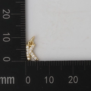 Macro di un ciondolo a lettera K dorato con zirconi e scala di misurazione reale