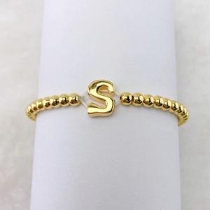 Detail eines 18k vergoldeten Perlenarmbands mit einem runden metallischen S-Anhänger
