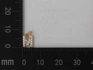 Dettaglio ciondolo lettera M dorata con zirconi e righello che mostra 10mm