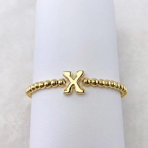 Detailansicht eines goldfarbenen Perlenarmbands mit poliertem Buchstaben X Anhänger