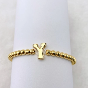 Detailansicht eines goldfarbenen Perlenarmbands mit einem metallischen Buchstaben-Y-Anhänger