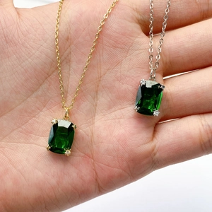 Gold and silver necklaces with square green emerald-cut zircon pendants held in hand
