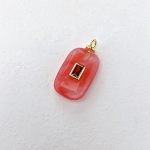Macro detail of a rectangular pink gemstone pendant with an inlaid red crystal charm