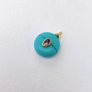 Detail of round turquoise donut pendant with purple gemstone and gold bezel