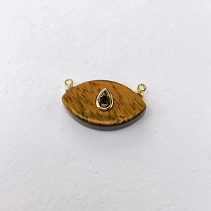 Detail of eye-shaped tiger eye stone pendant with green gemstone and gold plating