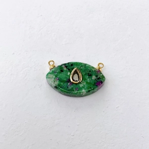 Macro detail of eye-shaped Ruby Zoisite pendant with gold trim and drop stone inlay
