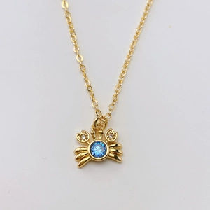 Dettaglio del ciondolo a granchio con gemma blu su una collana a catena dorata