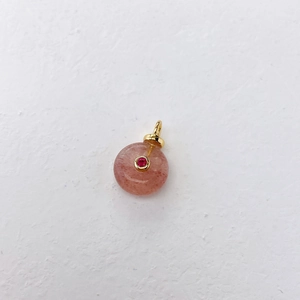Detail of round pink natural gemstone pendant with gold ring and small red center stone