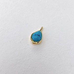 Macro detail of teardrop blue stone pendant with gold metal edging and closed hook