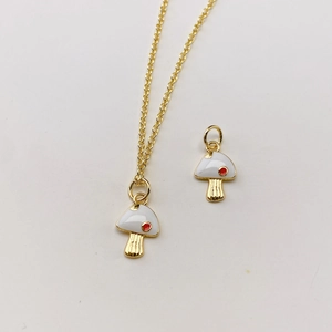 Nahaufnahme vom goldenen Pilzanhänger mit weißer Emaille und rotem Punkt Detail