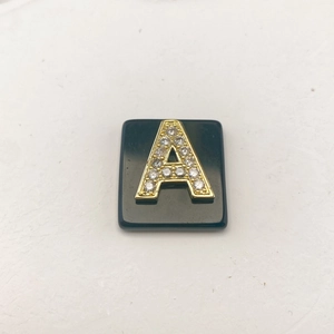 Detailansicht eines schwarzen Steinanhängers mit goldenem Buchstaben A und Strasssteinen
