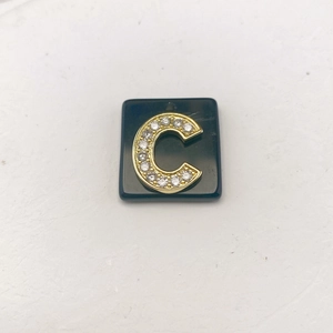 Makroaufnahme von Goldbuchstabe C Anhänger mit Strass auf quadratischem schwarzem Stein