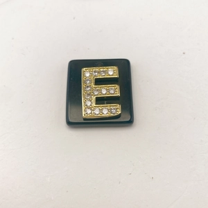 Detailansicht eines schwarzen Steinanhängers mit goldenem Buchstaben E und funkelndem Zirkon