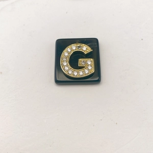 Makroansicht eines quadratischen schwarzen Onyx-Anhängers mit goldenem Pavé-Buchstaben G