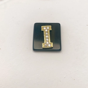 Detailansicht des schwarzen Steinanhängers mit goldenem Buchstaben I und Mikro-Kristallen