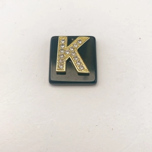 Nahaufnahme des schwarzen quadratischen Anhängers mit goldenem Buchstaben K und Kristallen