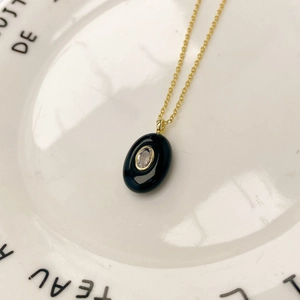 Détail d'un collier chaîne dorée avec pendentif ovale noir et pierre en zircone claire