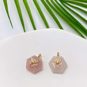 Detail of hexagon rose quartz pendants with gold butterfly charms on white ceramic plate