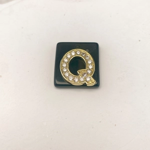 Nahaufnahme des goldenen Buchstaben Q Anhängers mit funkelnden Zirkonia auf schwarzer Basis