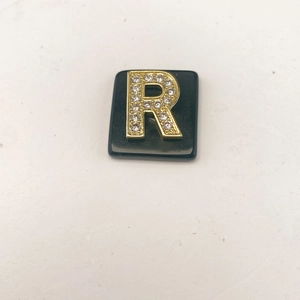 Detailansicht des goldenen Buchstabens R mit Strasssteinen auf schwarzem Naturstein