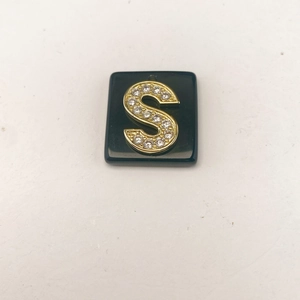 Detailansicht eines quadratischen schwarzen Anhängers mit goldenem Buchstaben S und Zirkonia